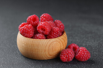 Close up, macro of fresh red ripe raspberries in rustic wooden bowl on dark textured background. Natural, organic fruit still life for healthy lifestyle and clean eating themes. High contrast.