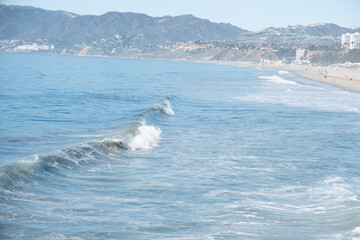 Foamy waves roll steadily onto the sandy shoreline along Santa Monica&rsquo;s coast with bright sunshine overhead