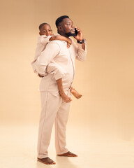 A cheerful African father carries his smiling son on his back while talking on the phone. In...