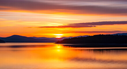 Obraz premium serene sunset panorama: calm lake, silhouetted mountains, vibrant sky