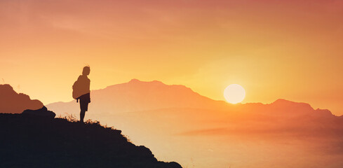 Naklejka premium Alone man on mountain looking out into the distant sunset 