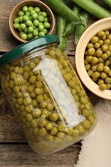Pickled peas in jar and pods on wooden table, flat lay