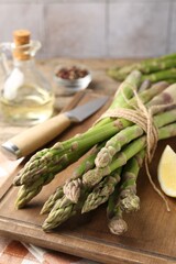 Fresh raw asparagus spears, knife and lemon on table, closeup