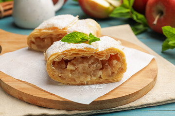 Pieces of tasty apple strudel with powdered sugar, mint and fruits on light blue wooden table, closeup
