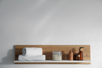 Wooden shelf with cosmetic products and towels on white background. Space for text