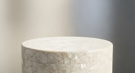 A cylindrical display stand with a mosaic tile surface, perfect for showcasing products. Soft lighting creates a serene atmosphere.