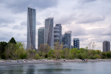 Summer view on Humber Bay Shores skyline from waters of Lake Ontario with people on the beach before modern high-rise buildings in background under evening cloudy sky. Humber Bay Shores is a historic
