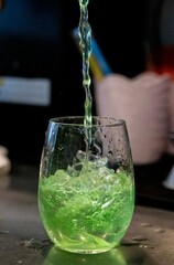 Green soda being poured into a clear glass with ice cubes and bubbles for a refreshing summer beverage