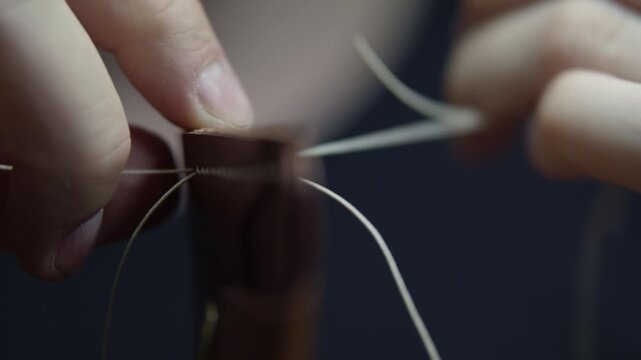 Close-up of a skilled leather craftsman hand stitching leather with a saddle stitch.