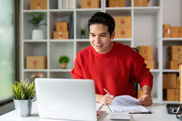 Fototapeta premium E-commerce Success. Smiling young man reviewing documents in home office.