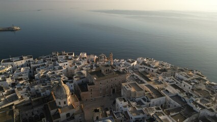 Coastal Town at Sunrise: An aerial view of a coastal town bathed in the soft glow of the rising sun, with buildings and architecture stretching towards the sea. Monopoli, Puglia