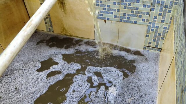 Overflowing water filled with dirt and bubbles in a tiled basin, highlighting pollution.