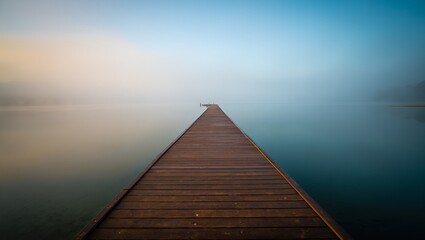 Fototapeta premium A serene wooden pier stretches into a misty lake at dawn, creating a tranquil and calming scene.