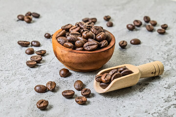 Close up view of roasted coffee beans on the little or small wooden bowl and wooden scoop. scattered on grey or gray cement as background.