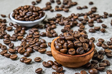 Close up view of roasted coffee beans on the little or small wooden bowl and white plate. scattered on grey or gray cement as background.