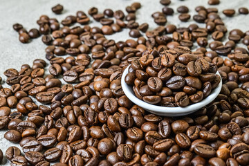 Close up view of roasted coffee beans on the little or small white plate. scattered on grey or gray cement as background.
