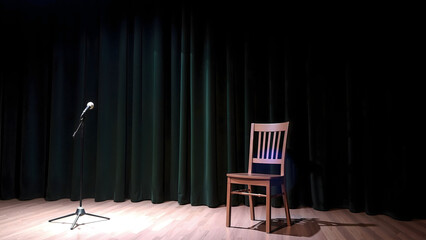 Empty stage with closed curtain, with illuminated microphone and old chair. Green curtain with podium with empty copy space. Background.