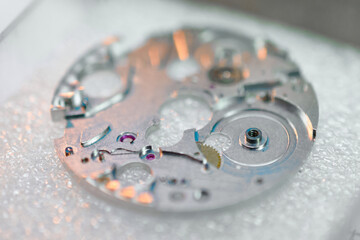 Intricate details of a precision watch mechanism base in a watch factory surrounded by artisans