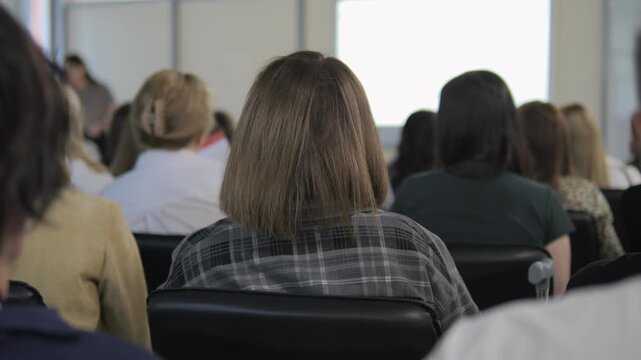 Group of people are sitting in a classroom. A woman is standing in front of a projector screen