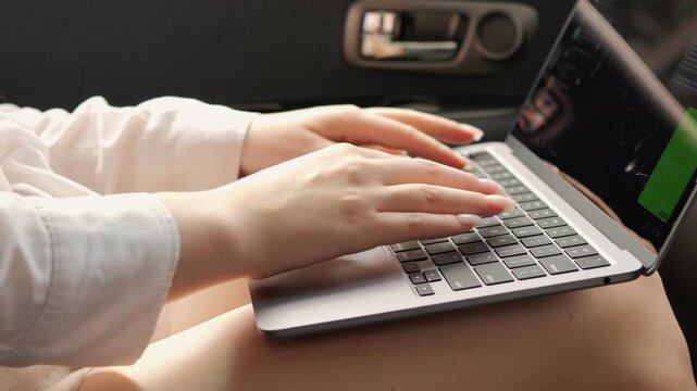 Woman is typing on a laptop. The laptop is open and the screen is green. The woman is sitting on the floor