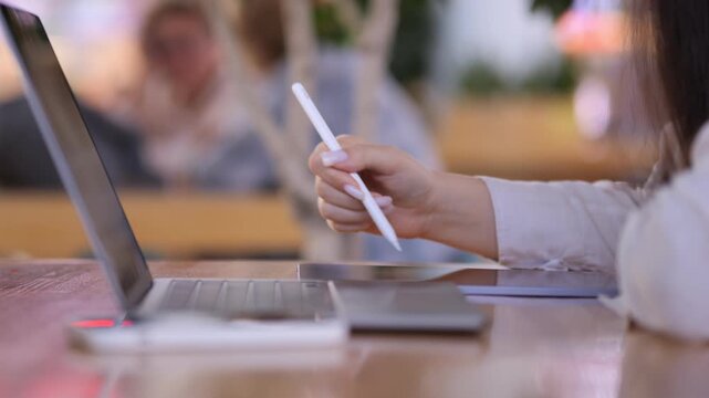 Woman is writing on a laptop. She is using a white pen. The laptop is on a table