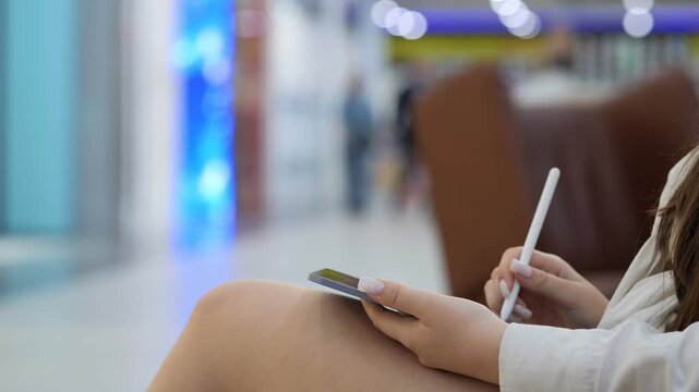 Woman is sitting on a couch with a cell phone in her hand. She is also holding a pen