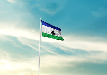 Lesotho flag is waving on a tall flagpole among the clouds. Lesotho national flag for independence day.