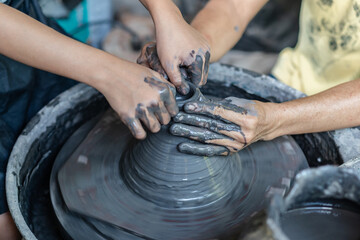 A pottery artist's hands guide a child's hands on the spinning potter's wheel.
