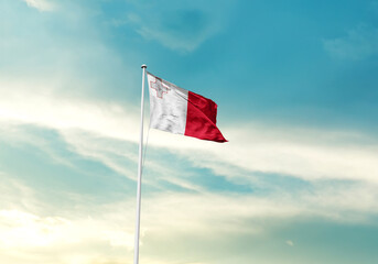 Malta flag is waving on a tall flagpole among the clouds. Malta national flag for independence day.