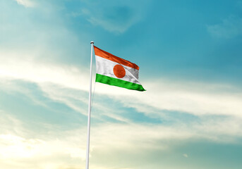 Niger flag is waving on a tall flagpole among the clouds. Niger national flag for independence day.
