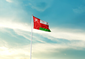 Oman flag is waving on a tall flagpole among the clouds. Oman national flag for independence day.