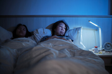 Asian single mum is sleepless near her daughter, stressed, and worried awake at night because of drug side effects, insomnia illness in bed, mature and menopausal woman, family healthcare problem.