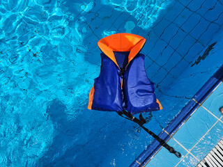Brightly colored life vest floats on surface of a clear blue swimming pool