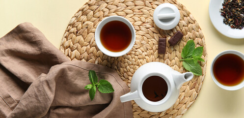 Beautiful composition with tea pot, cups of tea and wicker mat on beige background
