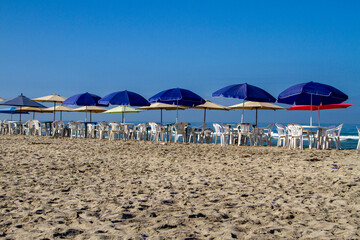 A horizontal view of umbrellas, tables and chairs on a beach set up for tourists