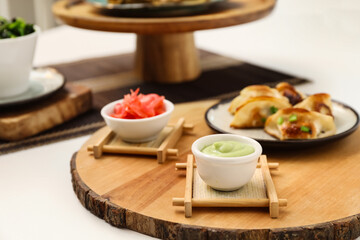 Wooden board with tasty Chinese jiaozi, wasabi and ginger on light background, closeup