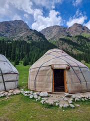 A traditional yurt camp located in the mountains of Kyrgyzstan. The picturesque gorge with green pastures and snowy peaks creates a unique atmosphere of nomadic culture and nature in Central Asia.