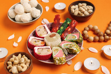 Candles with beads and plates of different treats on orange background. Divaly celebration