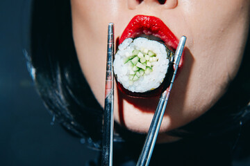 Close-up of a woman enjoying sushi, featuring bold red lips and chopsticks, highlighting a vibrant culinary experience with Asian cuisine.