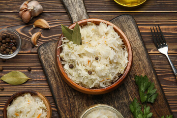 Bowls with delicious sauerkraut and different spices on wooden background