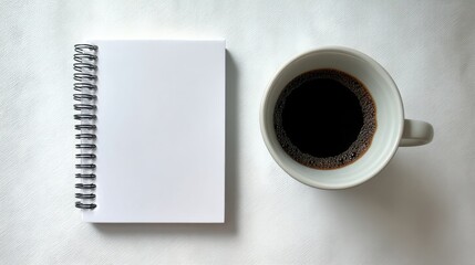 An open spiral bound notebook with blank pages sits beside a ceramic cup filled with black liquid resembling freshly bre