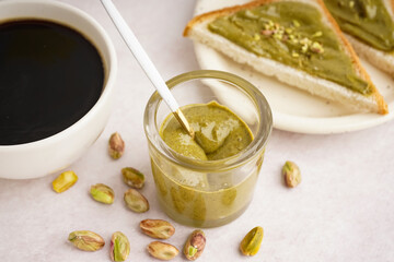 Glass with tasty pistachio paste and cup of coffee on light background