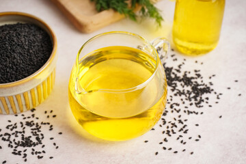 Jug of oil and bowl with sesame seeds on white background