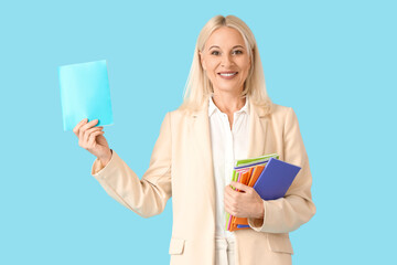 Mature female teacher with copybooks on blue background