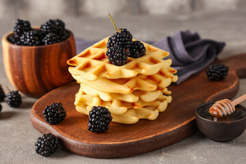 Delicious Belgian waffles with blackberry and honey on board on table against grey background. Closeup