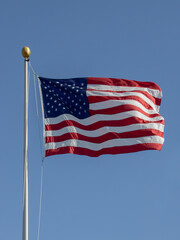 A photograph of the American flag waving proudly in the wind atop a flagpole, symbolizing national pride, freedom, and unity under a bright sky.