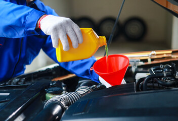 Mechanic pouring engine oil into car engine. Oil change service, car repair, engine inspection and maintenance.