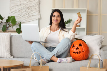 Young woman with credit card and laptop shopping online for Halloween at home