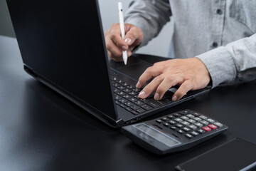 Businessman working on laptop with calculator and digital pen, concept of finance, accounting, and planning