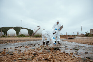 Two men in white protective suits are looking at a laptop. They are standing near a body of water. Wastewater testing, Wastewater treatment system, water quality testing